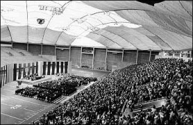 The UNI-Dome floor set up with a stage and chair for an event with a crowd in the bleachers.