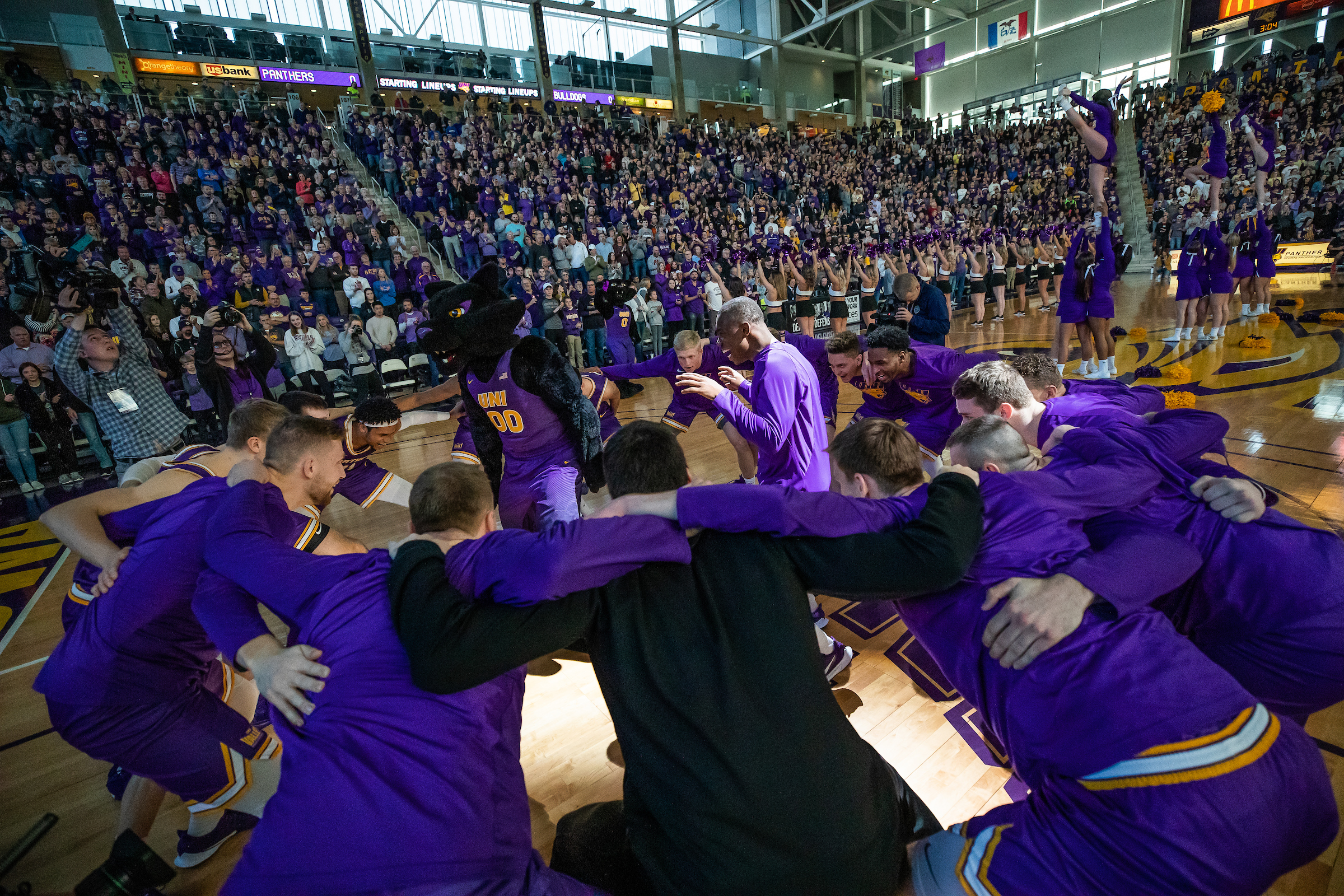 UNI Men's Basketball team huddling in a circle around TC.